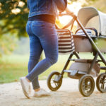 Woman with baby stroller walks in the park at sunset