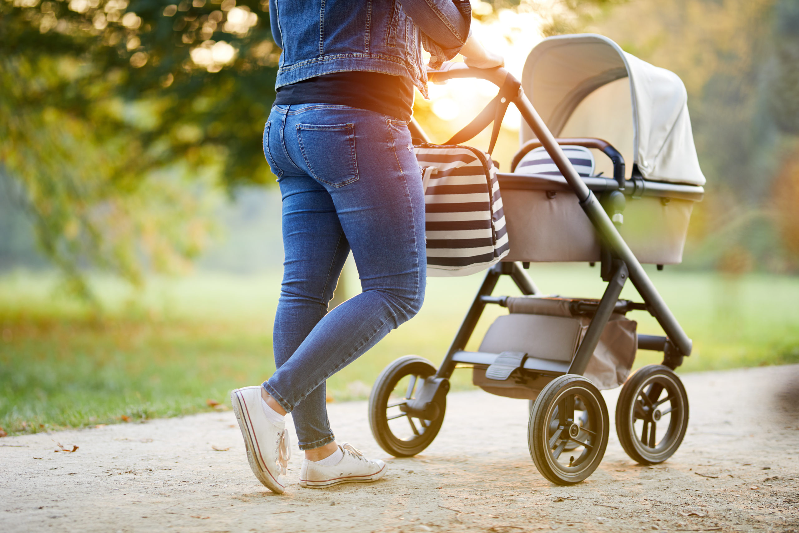 Woman with baby stroller walks in the park at sunset